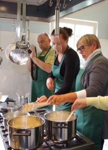 dames staan bij het fornuis in pannen te roeren bij workshop diner in kookstudio Sprankenhof